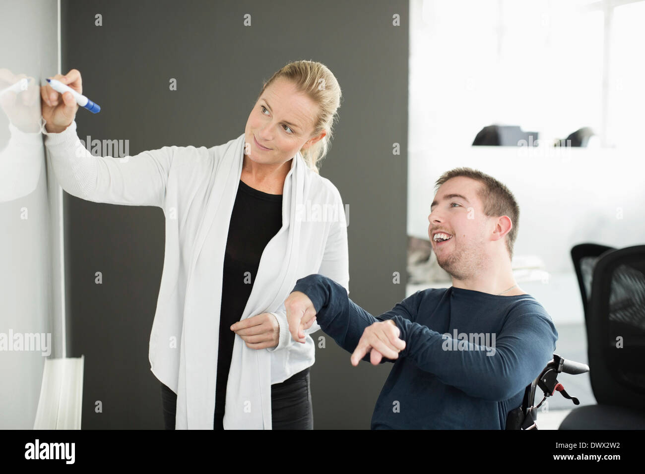 Businesswoman writing on whiteboard while working with disabled businessman in office Stock Photo