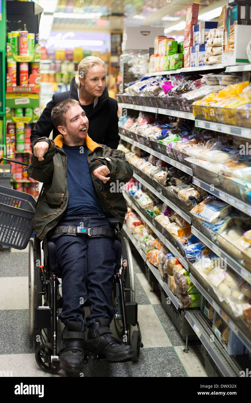 Disabled man on wheelchair shopping with caretaker in supermarket Stock