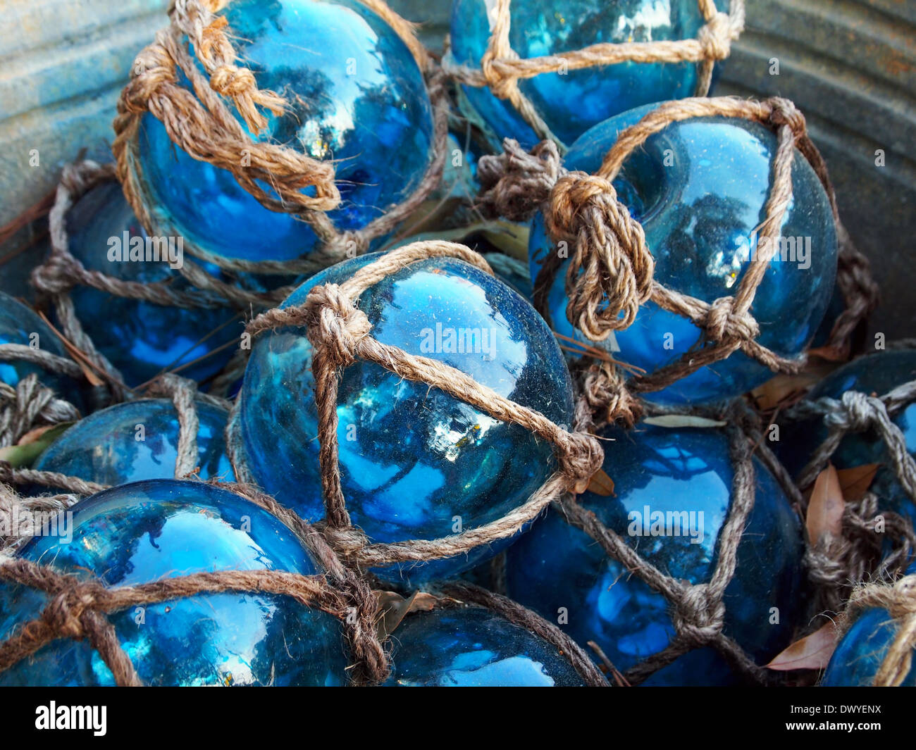 Glass fishing floats with rope knot netting piled in a bucket. Stock Photo