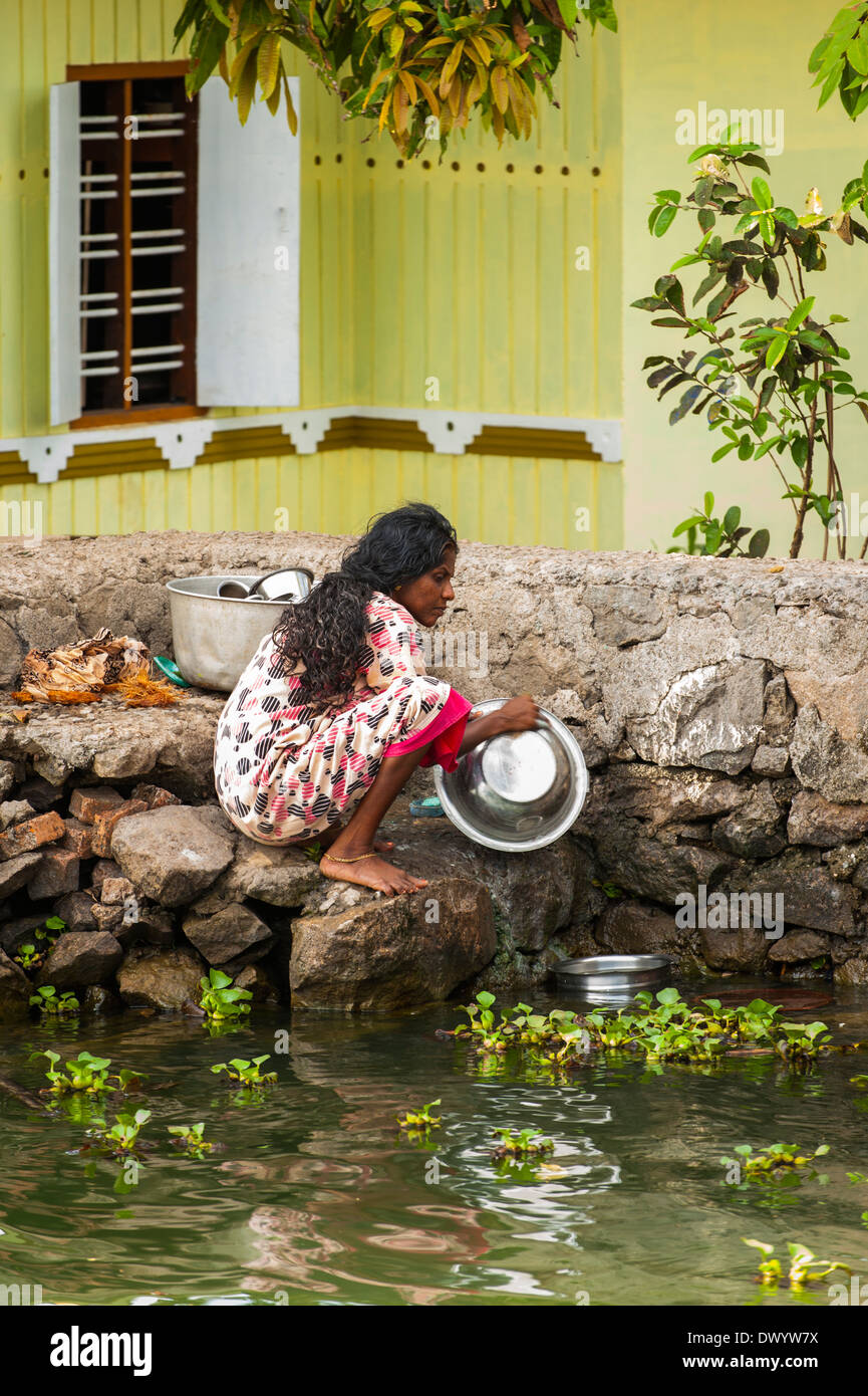 South Southern India Kerala backwater tour cruise waterway canal woman lady washing metal pots dishes in water by steps stairs Stock Photo