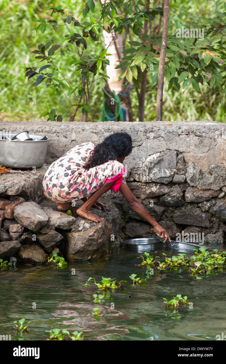 South Southern India Kerala backwater tour cruise waterway canal woman lady washing metal pots dishes in water by steps stairs Stock Photo