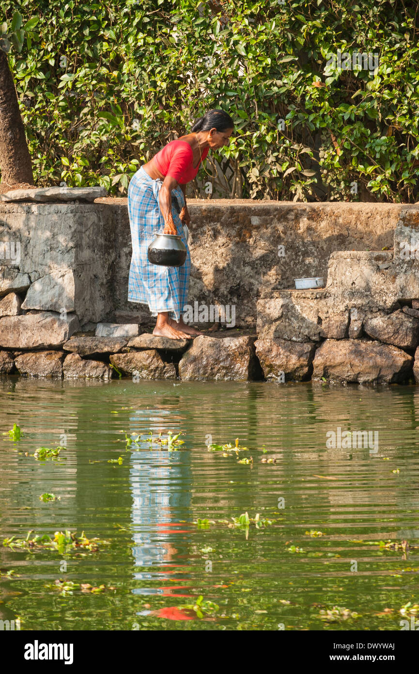 South Southern India Kerala backwater tour cruise waterway canal women washing up metal pots dishes in water by steps stairs Stock Photo