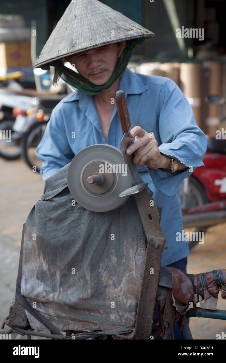 Knife Sharpener in Coolie Hat at Market in My Tho Town Market Vietnam Stock Photo