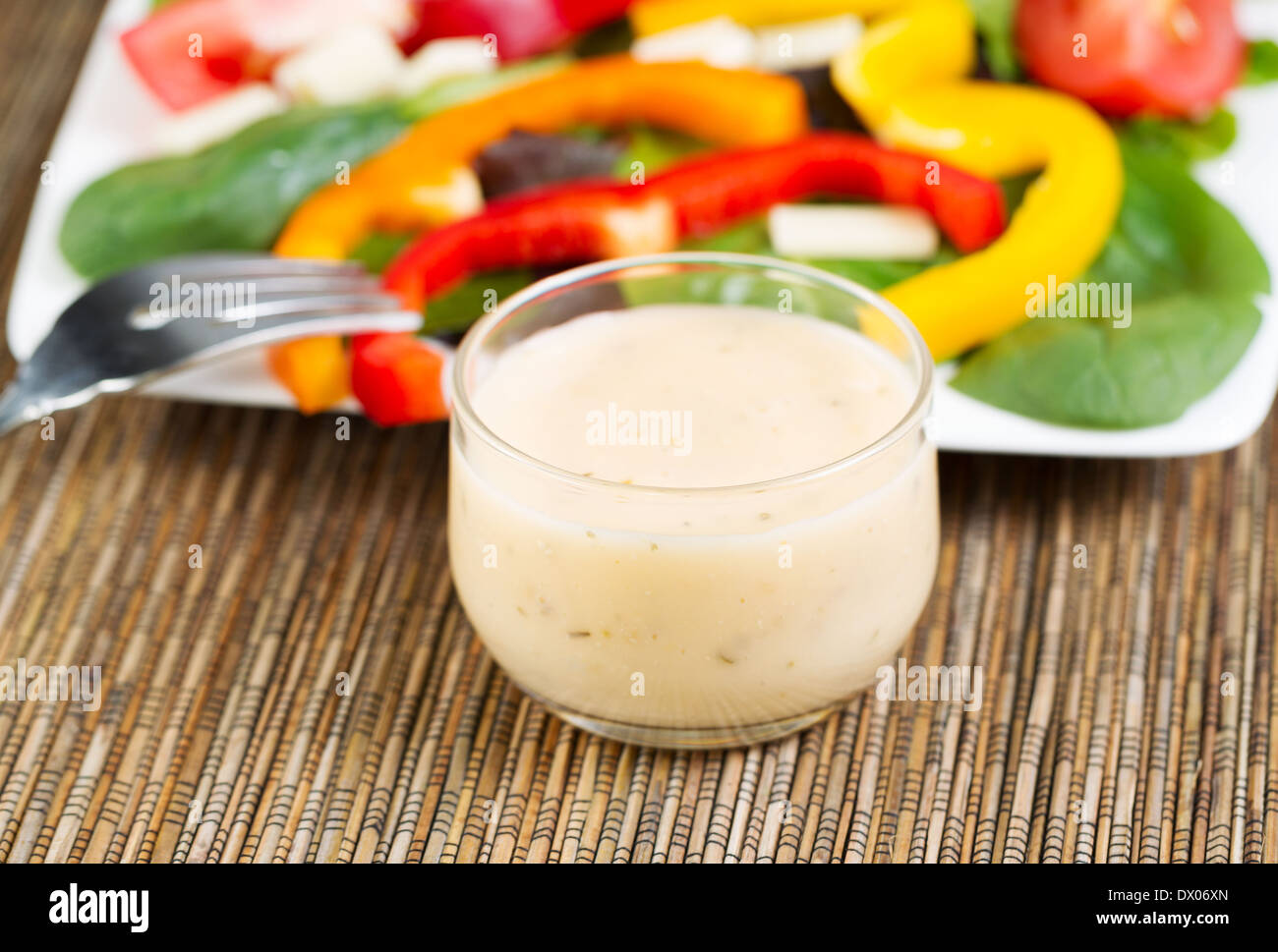 Horizontal photo of a small glass bowl filled with creamy Italian dressing with salad on white plate in background Stock Photo