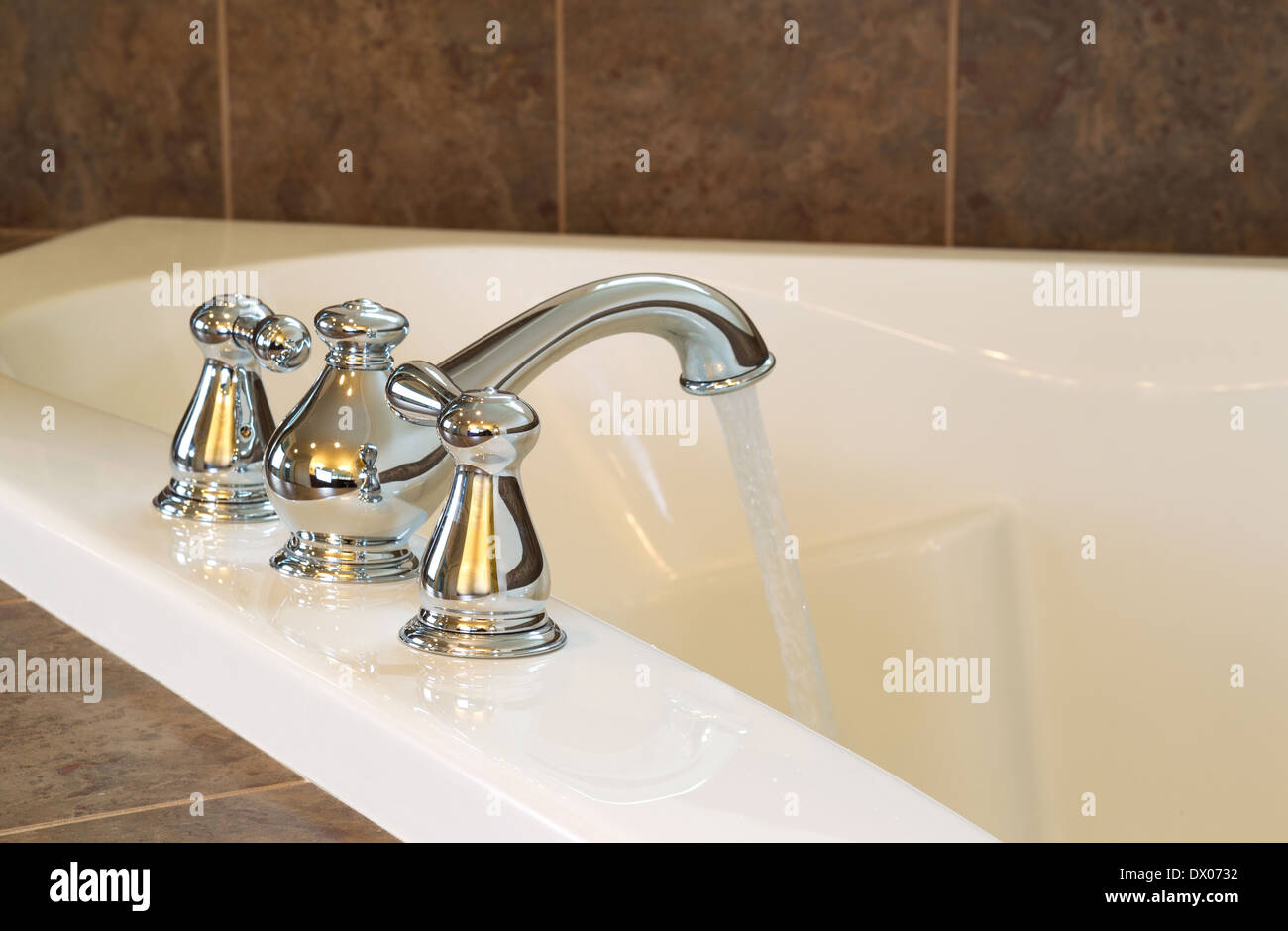 Closeup horizontal photo of chrome faucet running water into soaking tub in master bathroom Stock Photo