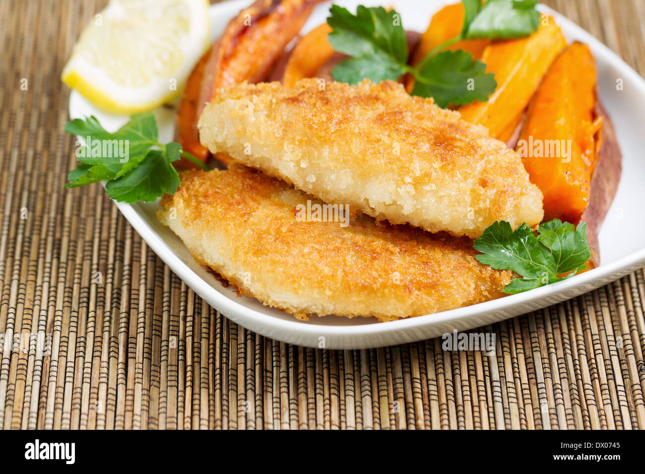 Closeup horizontal of golden crisp fried fish and yams in white plate with bamboo place mat underneath Stock Photo