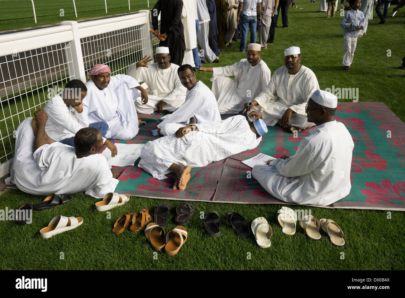 Men on carpet checking the form at horse racing meeting at Al Meydan racecourse at night in Dubai United Arab Emirates Stock Photo