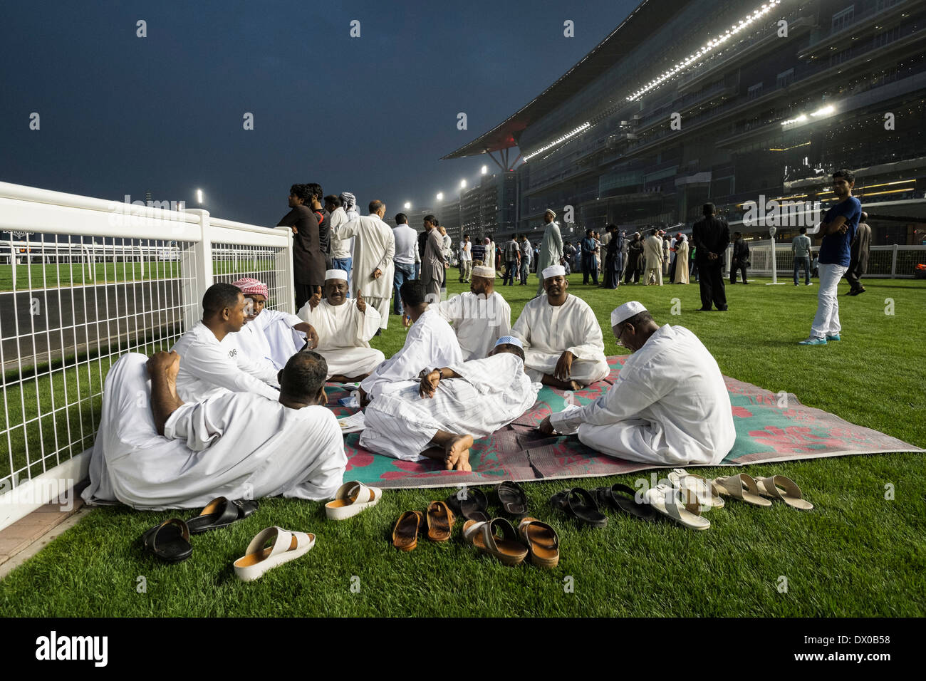 Men on carpet checking the form at horse racing meeting at Al Meydan racecourse at night in Dubai United Arab Emirates Stock Photo