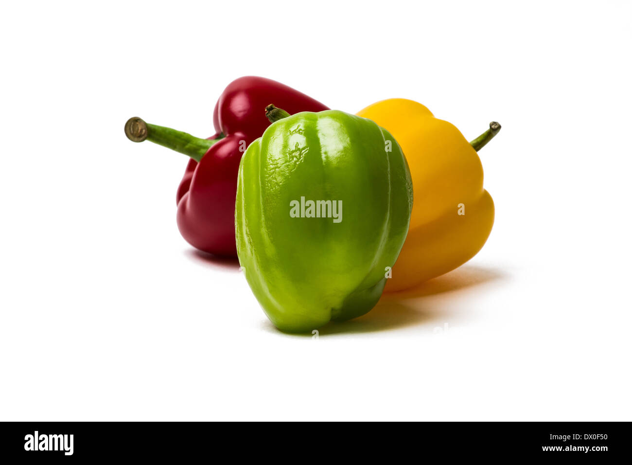 Three sweet peppers of red, yellow and green color. Green pepper is a main object. Two other peppers are behind it. Isolated. Stock Photo
