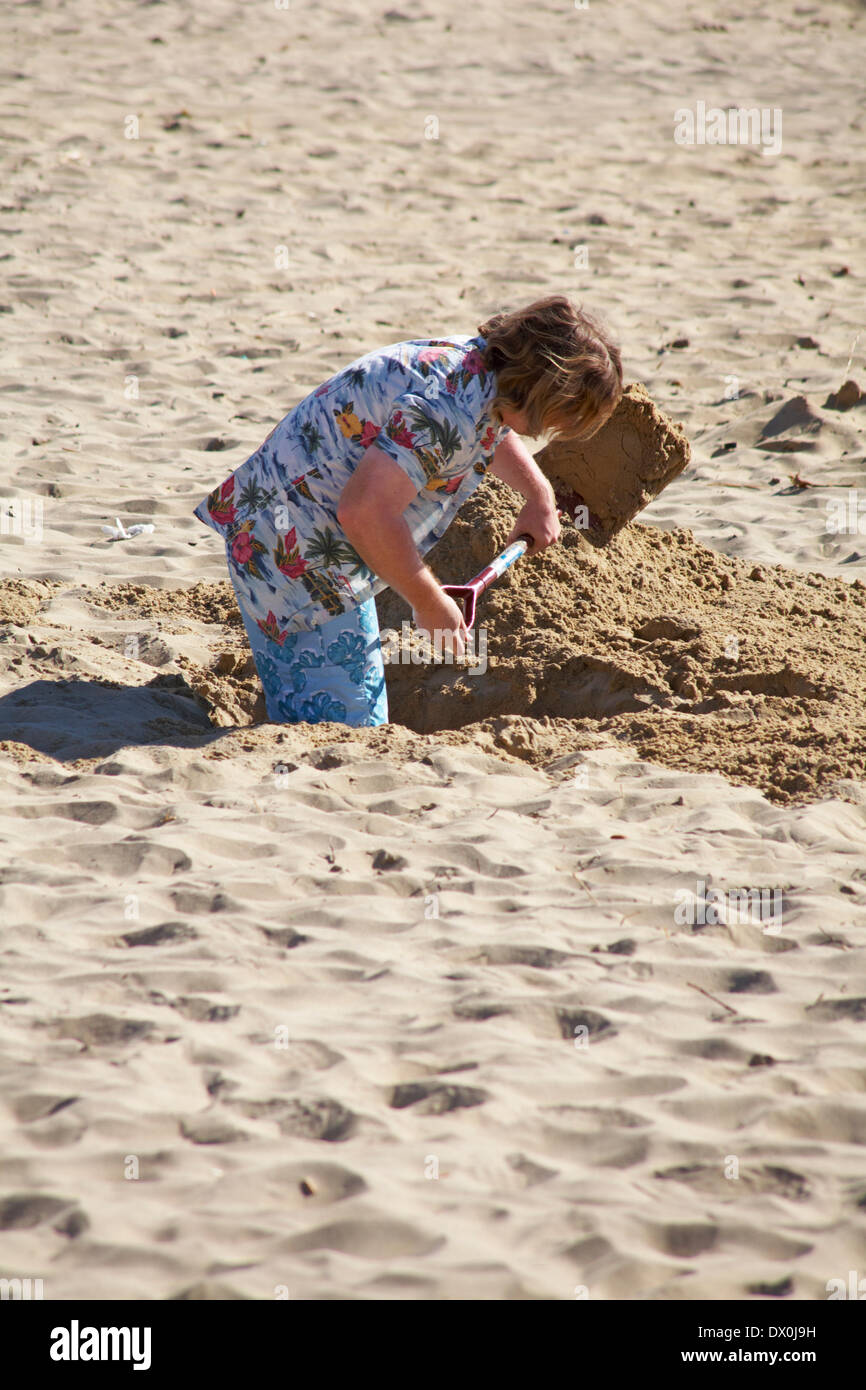 man digging a deep hole in the sand at Bournemouth beach, Bournemouth