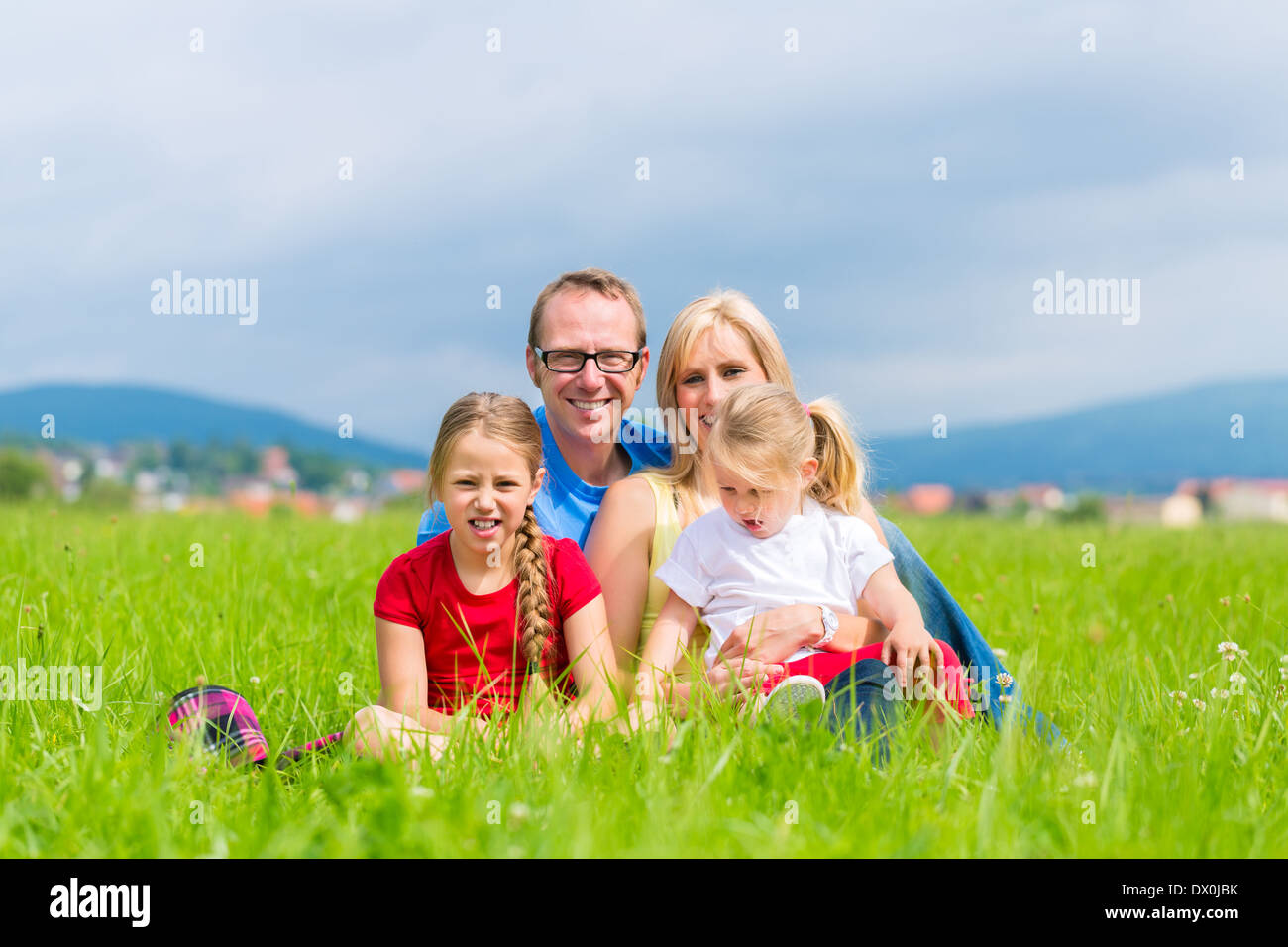 Happy family of Mother, father and kids or daughter and sisters or siblings sitting outdoor on meadow Stock Photo