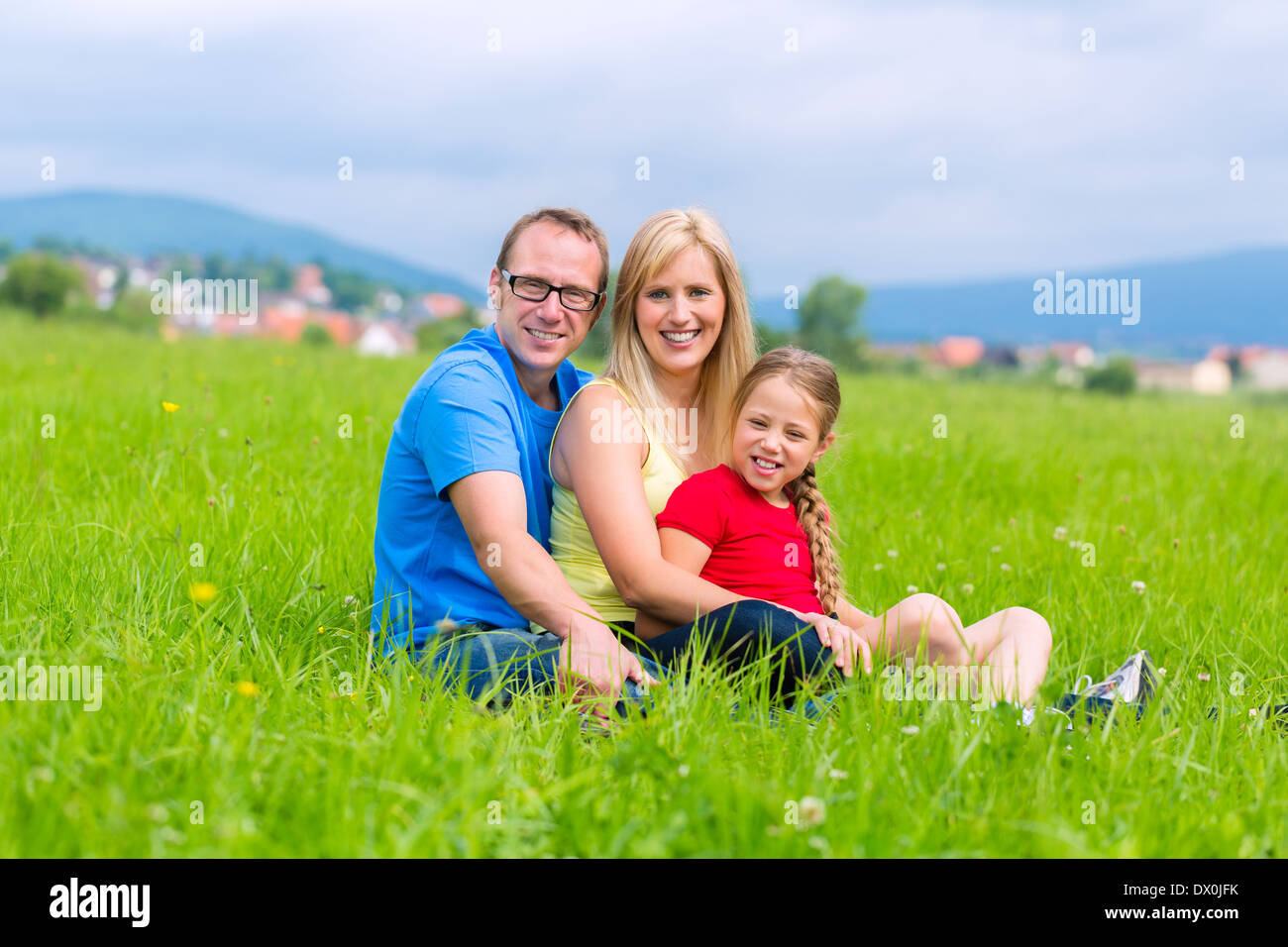 Happy family of Mother, father and kids or daughter and sisters or siblings sitting outdoor on meadow Stock Photo