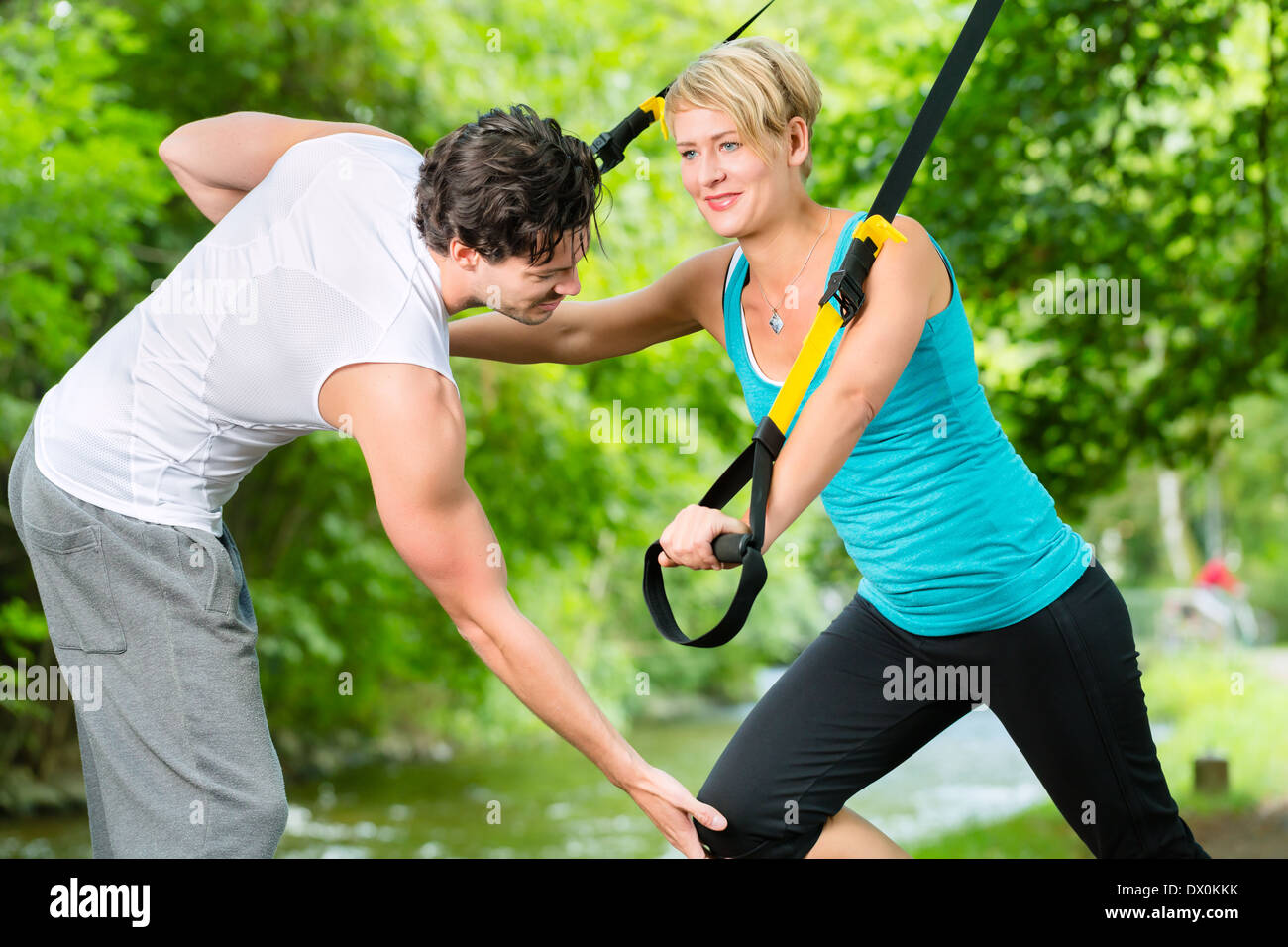 Fitness woman exercising with suspension trainer and personal sport trainer in City Park under summer trees Stock Photo