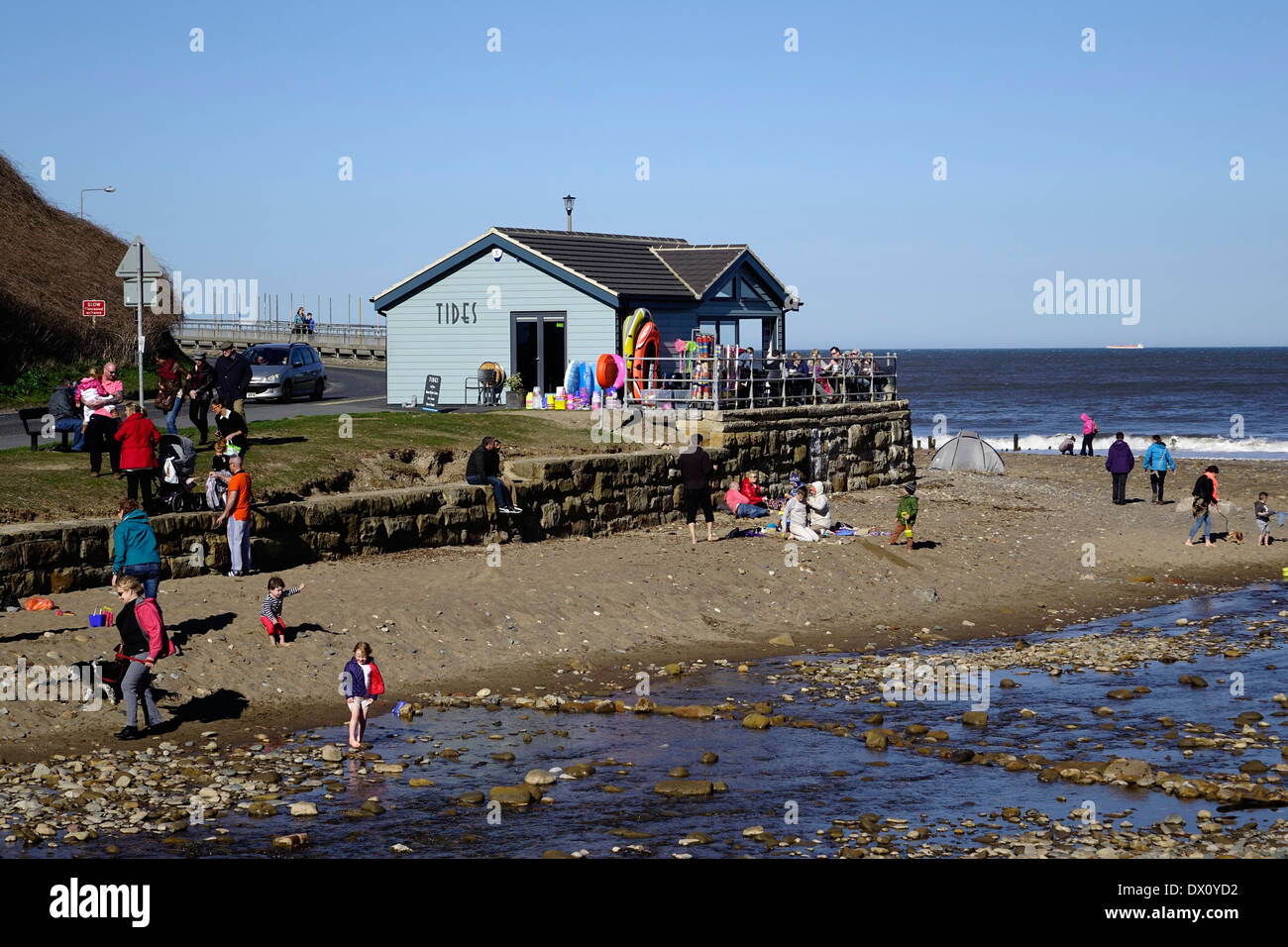 Holiday makers on the beach by the Tides café at Sandsend near Whitby North Yorkshire on a sunny but chilly spring day Stock Photo