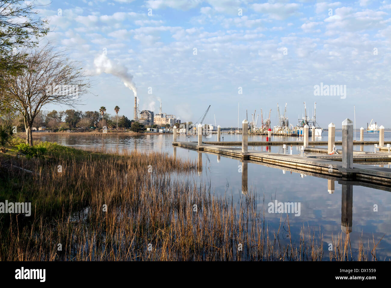 Fluffy white clouds (Altocumulus floccus) reflected in the still waters, trawlers at dock and a power plant in the distance. Stock Photo