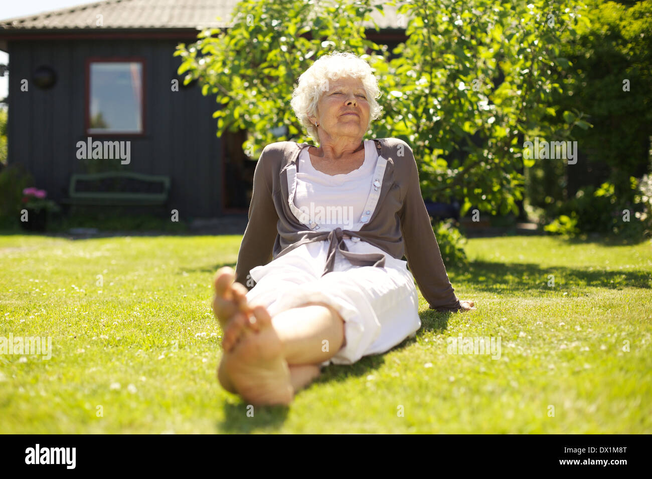 Senior woman sitting relaxed on grass in backyard garden outdoors Stock Photo