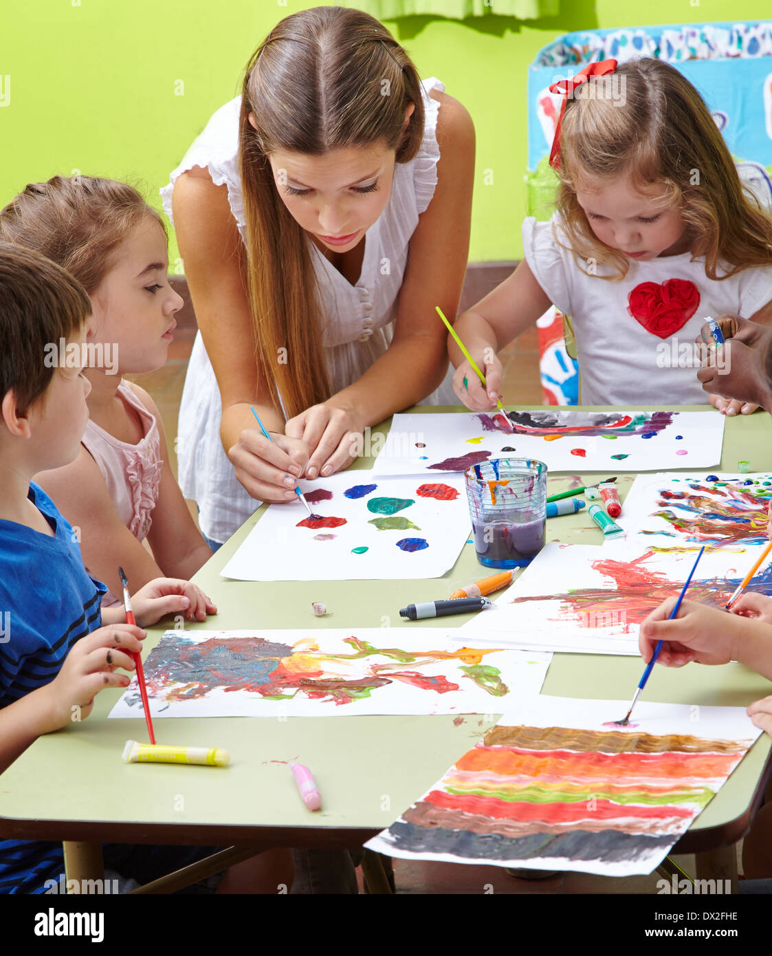 Nursery teacher painting with children and brushes and watercolor in ...