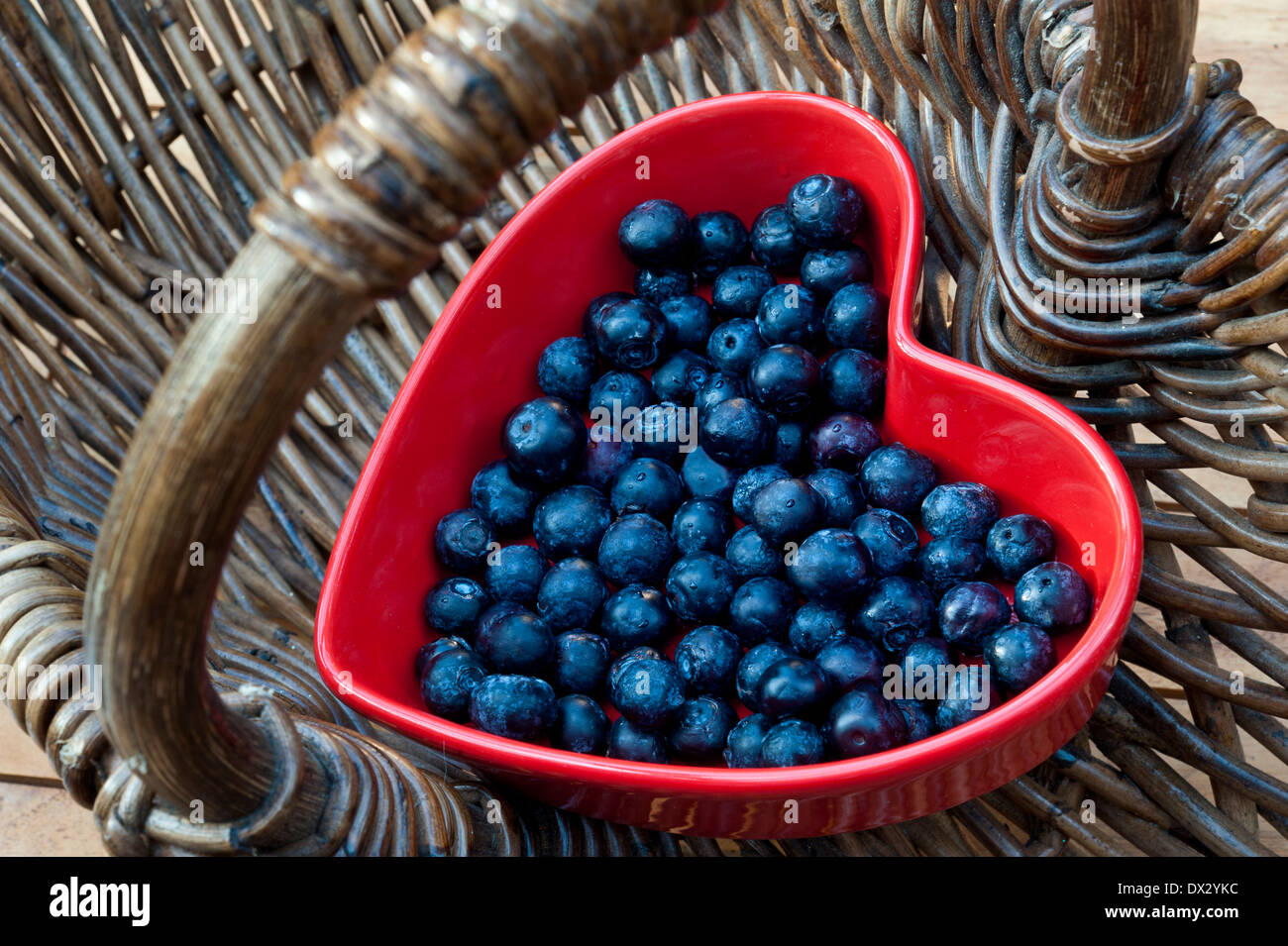 BLUEBERRIES HEART HEALTH BASKET SHOPPING Healthy food concept / Blueberries in a red heart shaped dish in a traditional wicker basket Stock Photo
