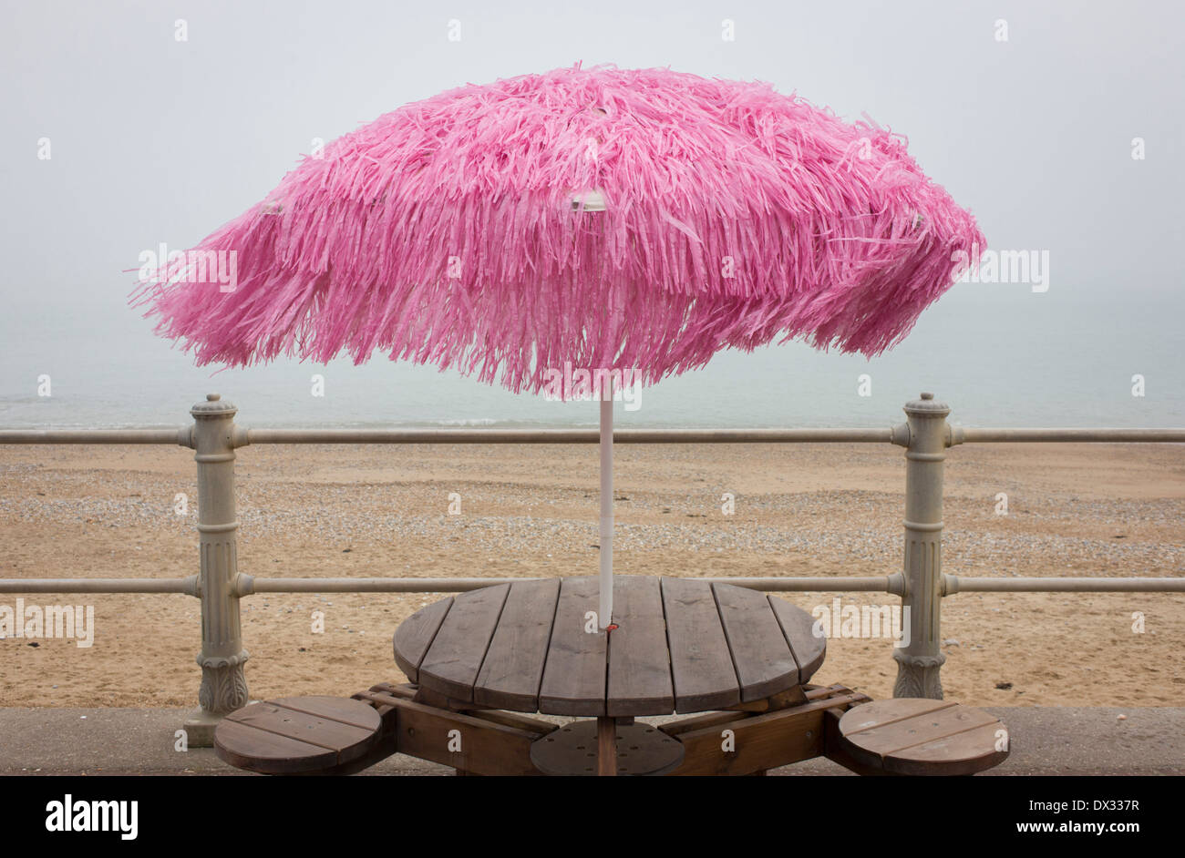 A pink-coloured parasol blows in the wind on a seafront during the winter  off-season Stock Photo - Alamy