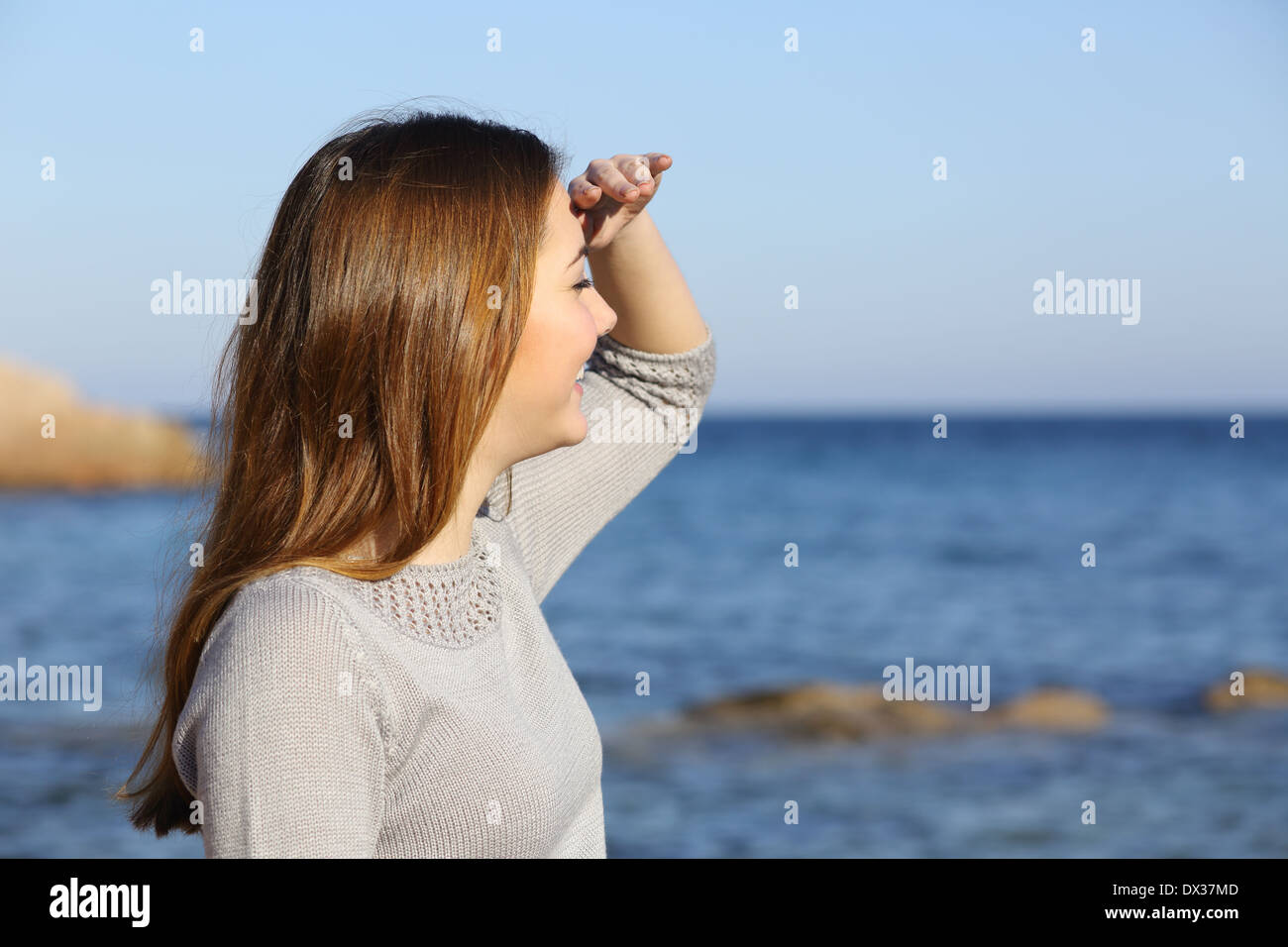 Happy woman on the beach looking forward at the horizon with her hand in forehead Stock Photo