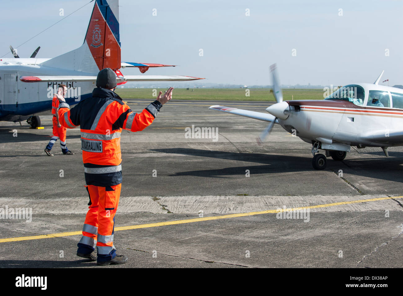 Marshaller giving directions to pilot in aircraft on runway at airport Stock Photo