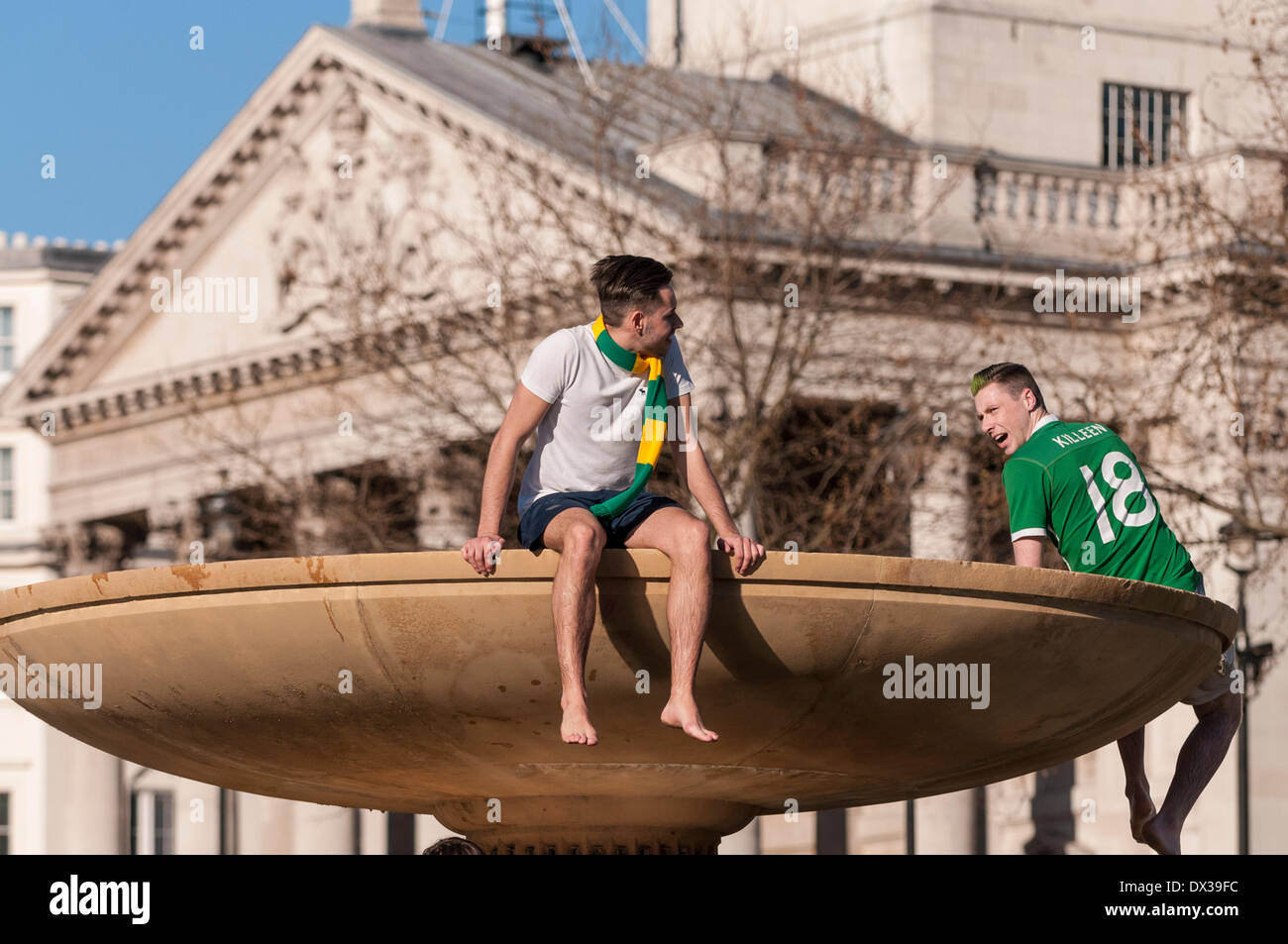Trafalgar Square, London, UK, 16 March 2014 - thousands of people gather in the square to celebrate St. Patrick's Day.  Two young men climb, illegally, one of the fountains in the square.  Credit:  Stephen Chung/Alamy Live News Stock Photo