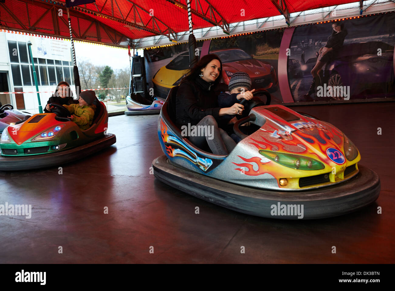 Little children with mother have fun in electric autoscooter - dodgem bumper car at fairground Stock Photo