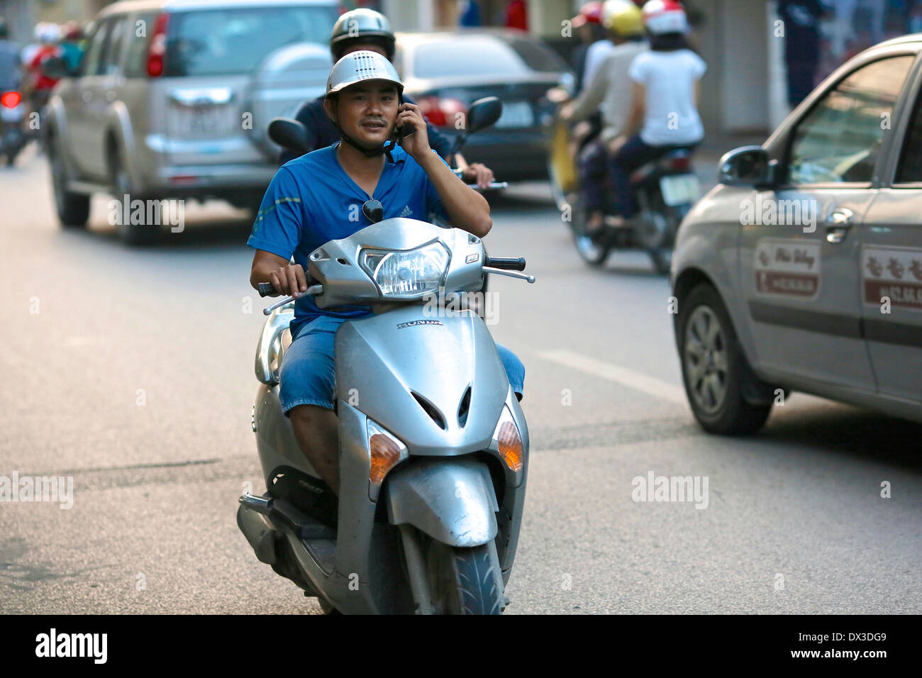 A young man uses a mobile phone whilst riding a scooter through the Old Quarter in Hanoi. Hanoi, Vietnam, Southeast Asia Stock Photo