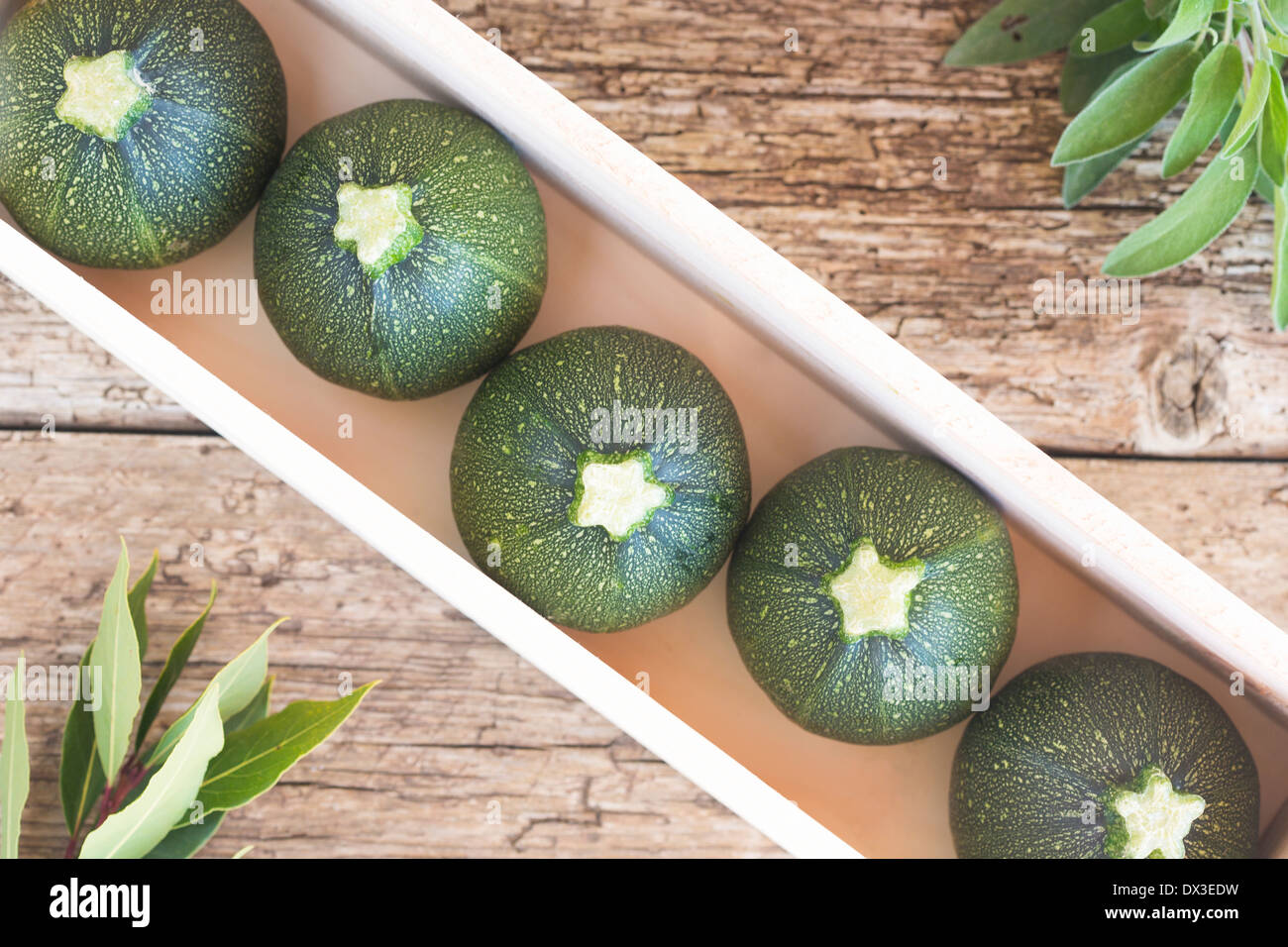 raw courgettes in wood box, with bay leaves and sage herbs on a rustic wood board Stock Photo
