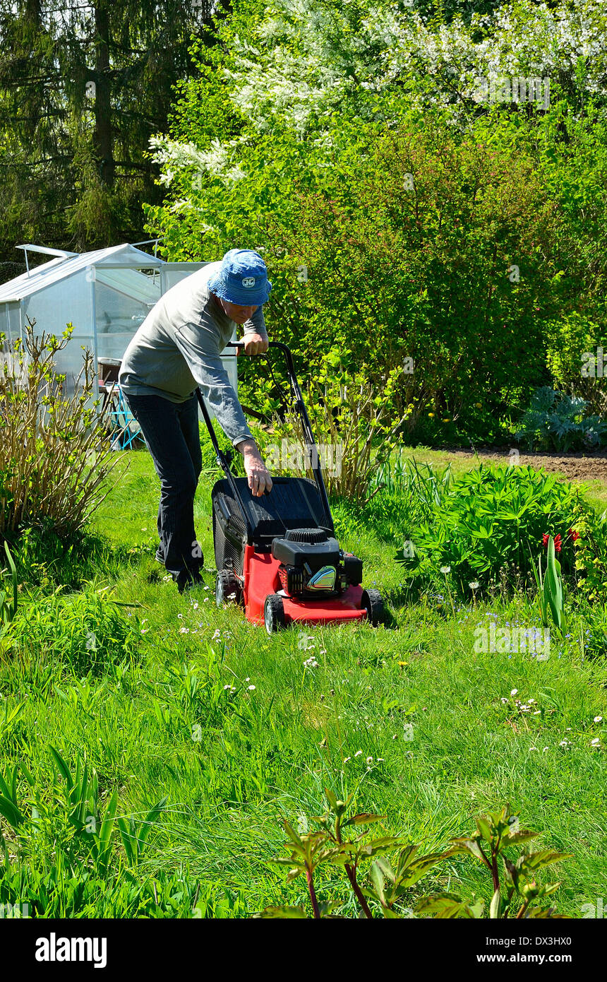 A man in a garden starts his lawnmower (Mayenne, Loire country, France). Stock Photo