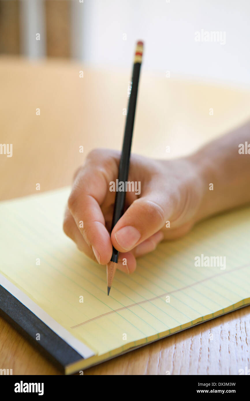 Man's hand holding pencil over legal pad at desk, close up Stock Photo