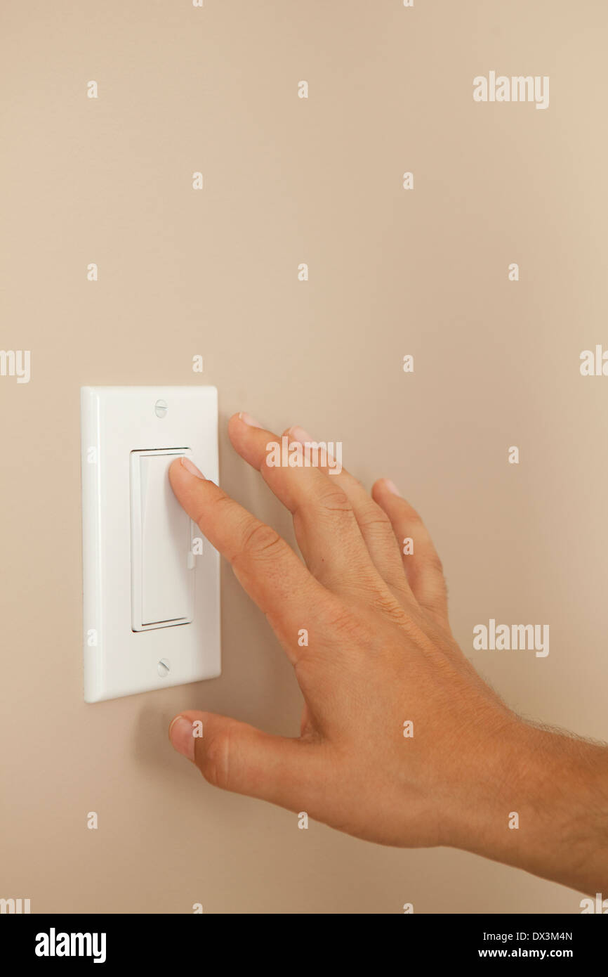 Man's hand turning on light switch on wall Stock Photo
