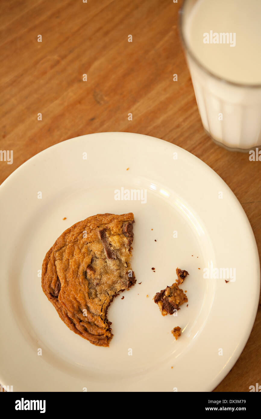 Homemade chocolate chip cookie with missing bites next to milk, directly above Stock Photo