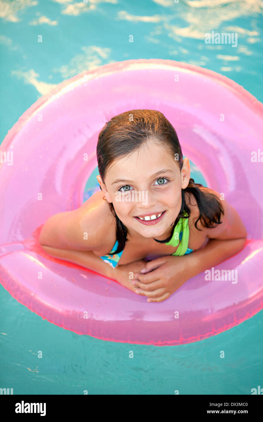 Smiling girl with wet hair inside of pink inflatable ring in swimming