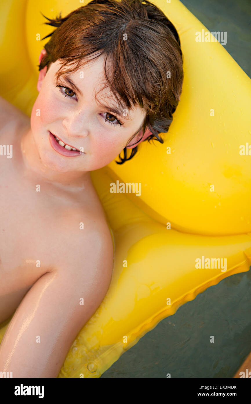Boy with wet hair on inflatable raft in swimming pool, portrait, high angle view Stock Photo