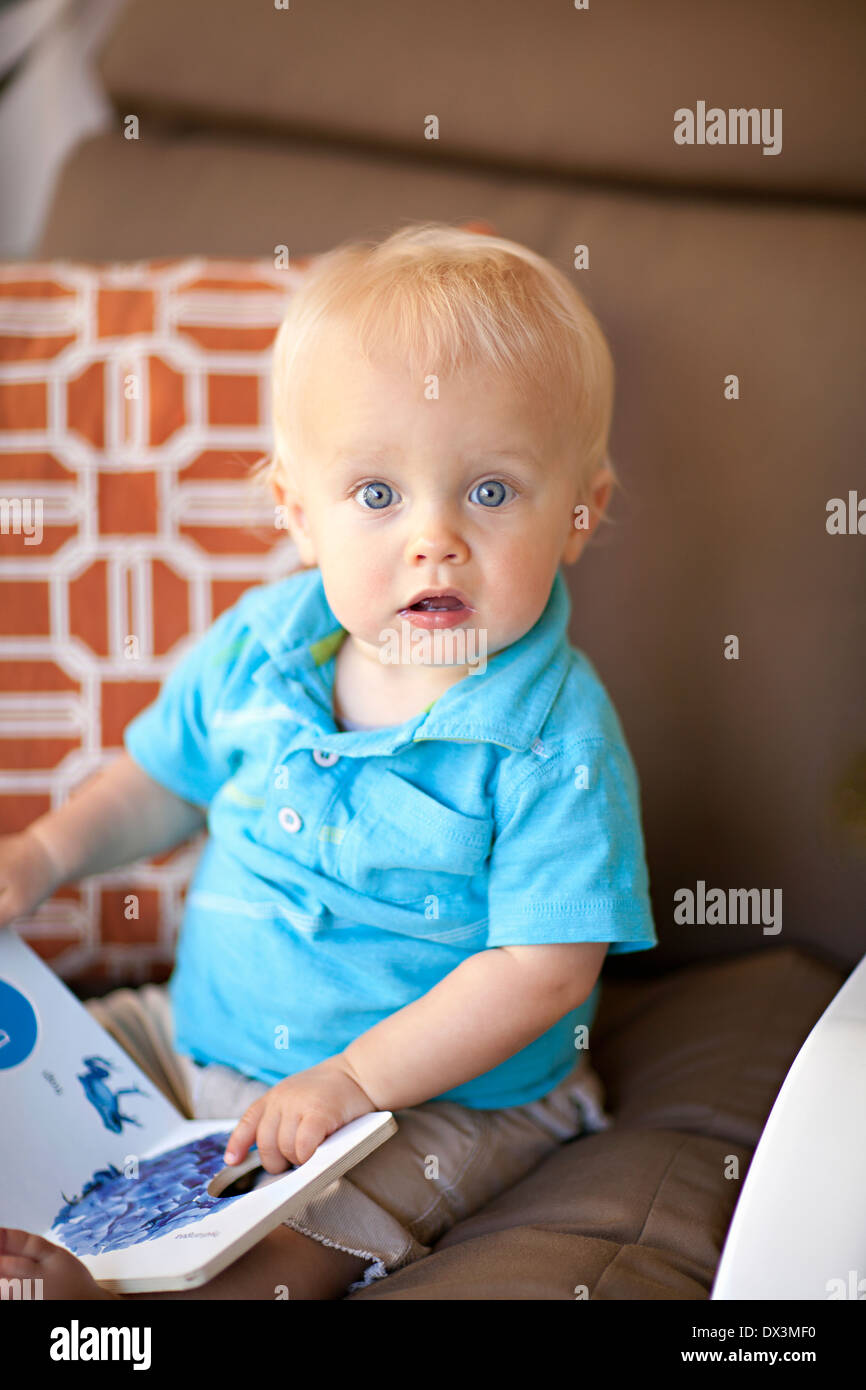 Surprised wide-eyed baby boy reading book, blonde hair, blue eyes, portrait Stock Photo