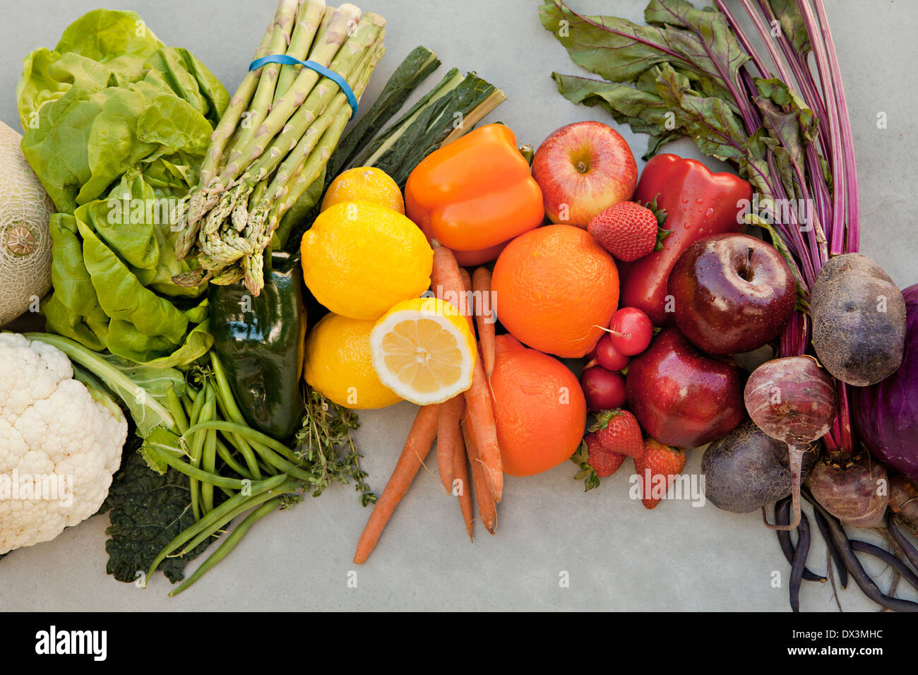 Abundant variety of multicolor fruits and vegetables organized by color on gray background, directly above Stock Photo