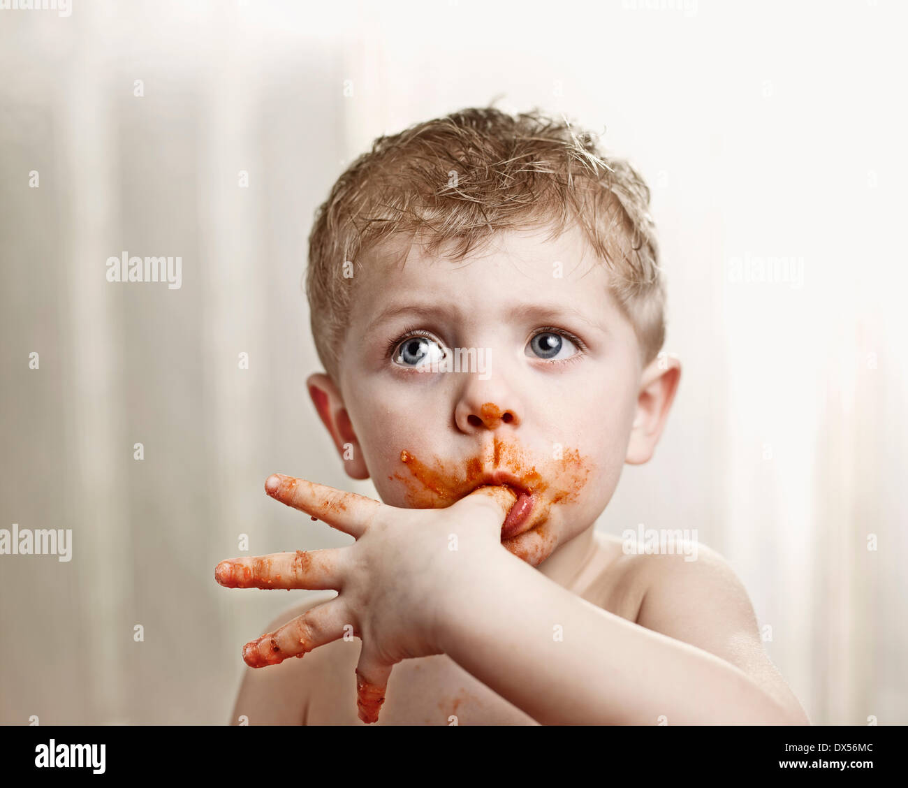 Toddler licking tomato sauce off his thumb Stock Photo