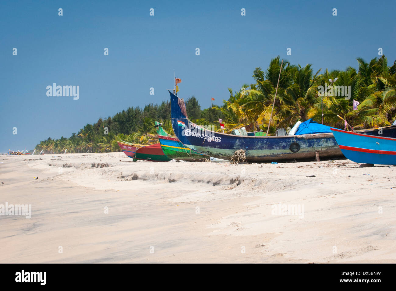 South Southern India Kerala Alleppy Mararikulam beach fishing boats wooden shore sand palm tree trees sun blue sky scene scenery Stock Photo