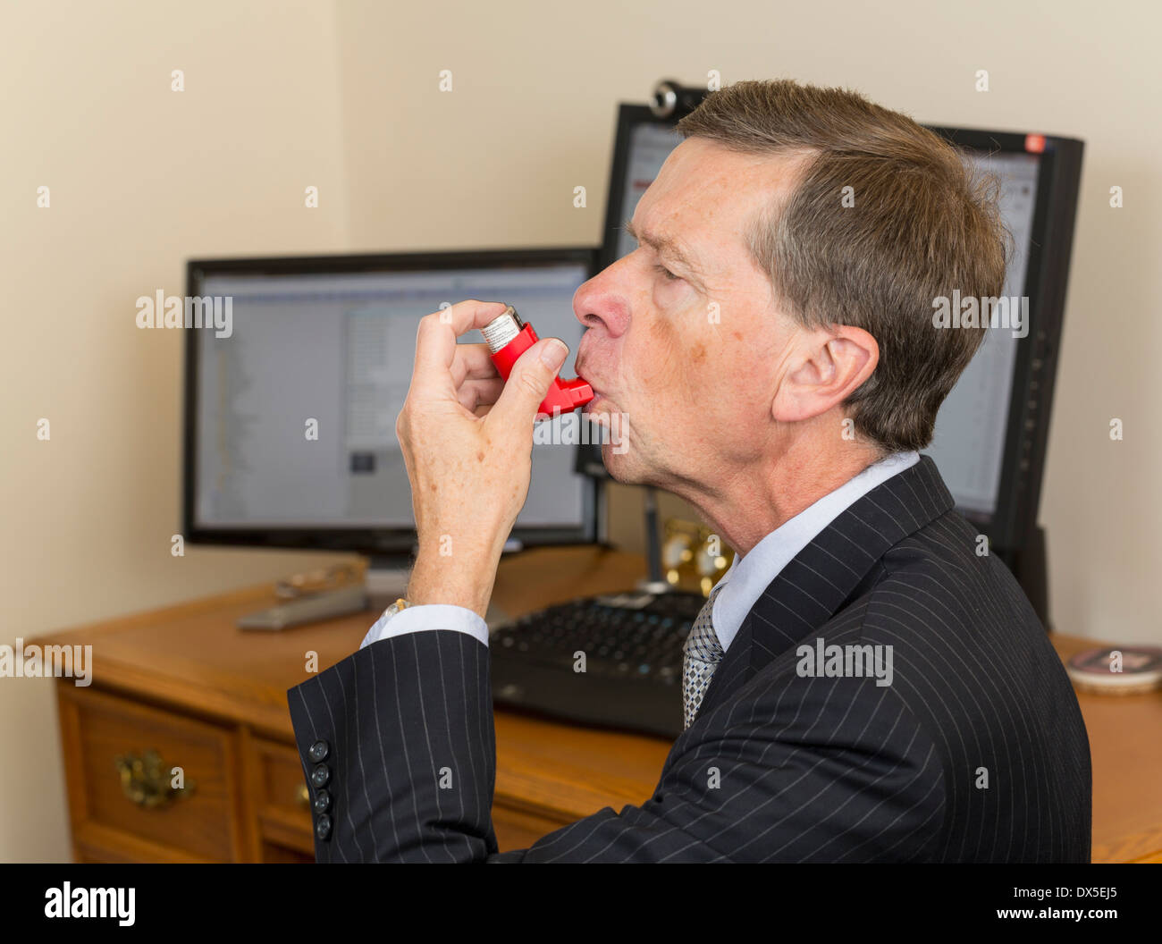 Businessman sitting at desk with computer screens using asthma inhaler Stock Photo