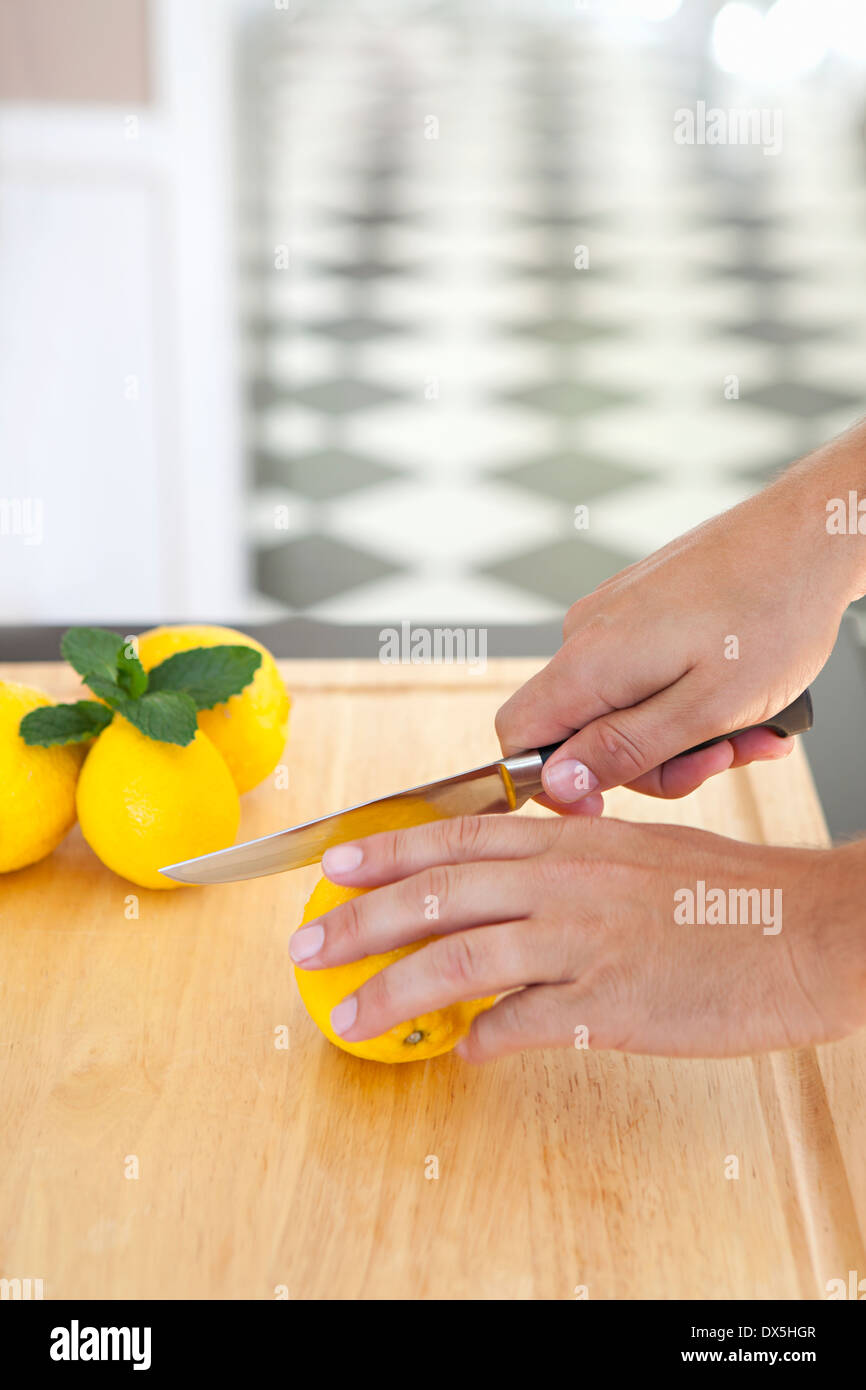 Man's hands slicing lemon on wooden cutting board in domestic kitchen, high angle view Stock Photo