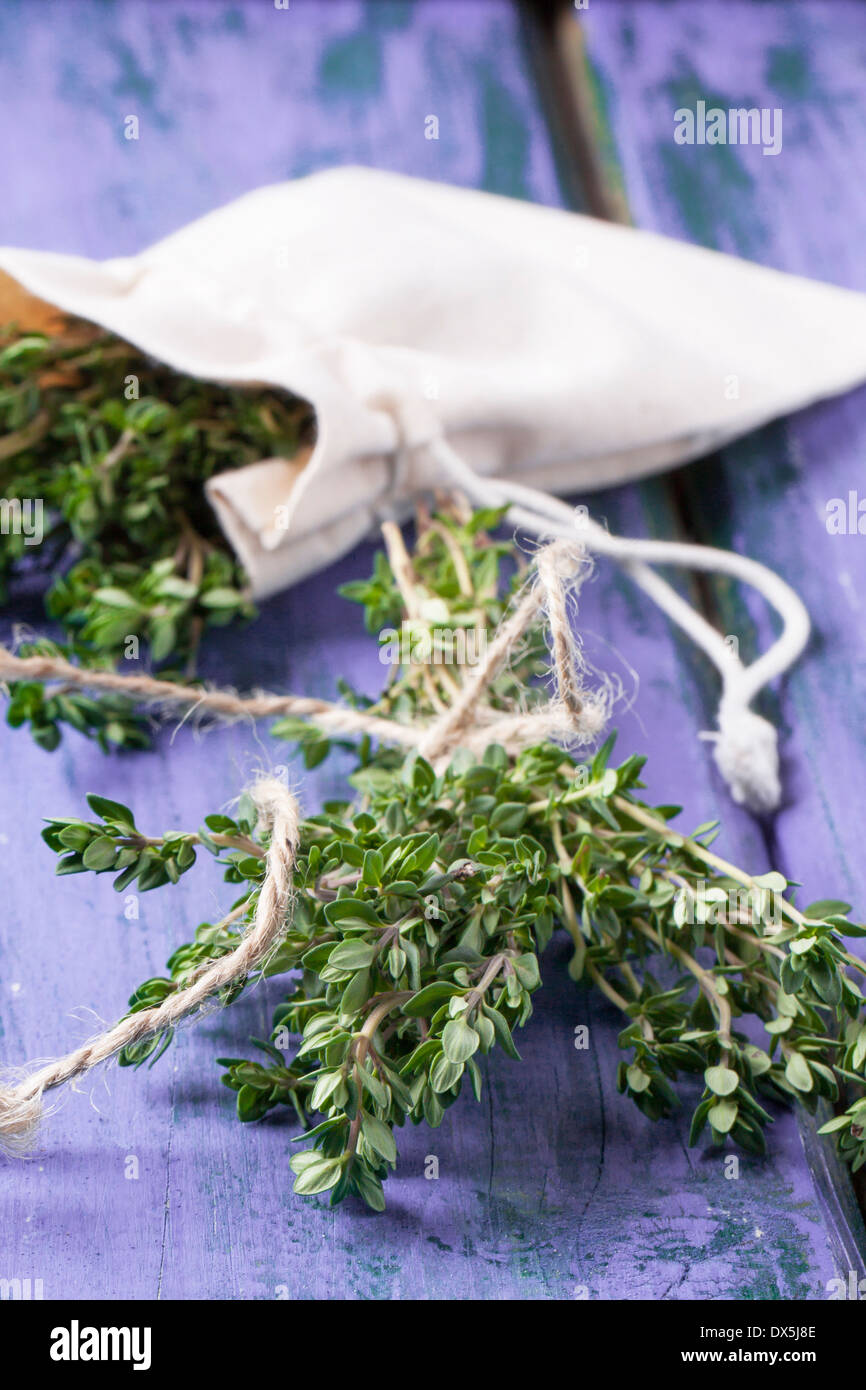 Bunch of fresh thyme and thyme in textile bag on violet wooden table Stock Photo