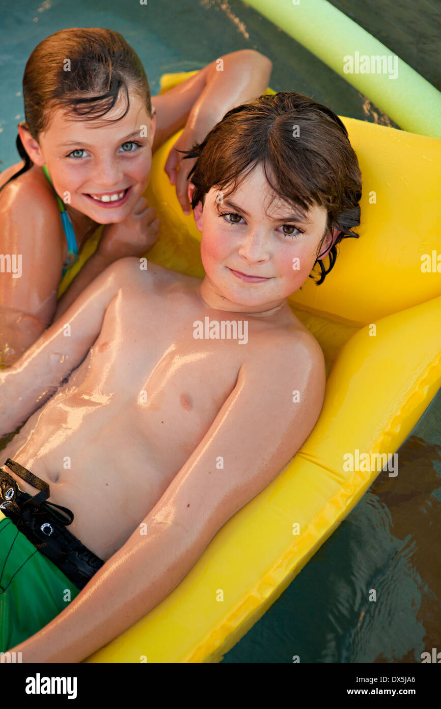 Boy and girl with wet hair on inflatable raft in swimming pool, portrait, high angle view Stock Photo
