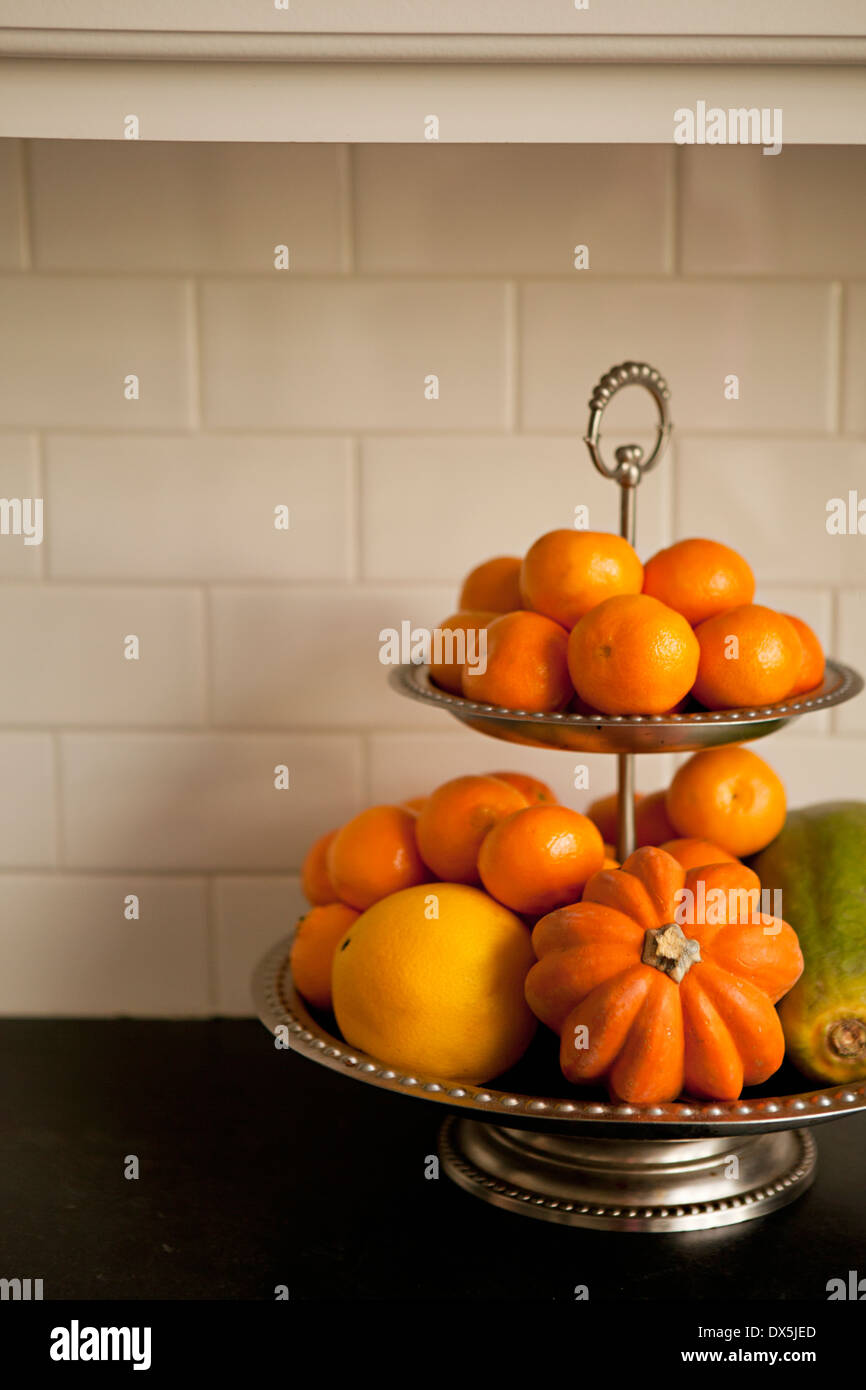 Tiered stand with orange fruits and vegetables on domestic kitchen counter, close up Stock Photo