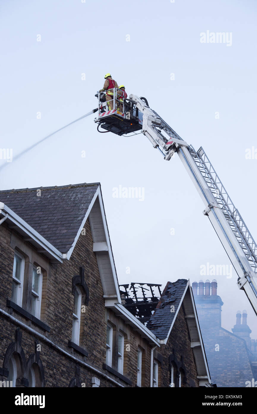 Brave firefighter crew (2 firefighters) up high ladder, tackle fire with water hose at town centre building - Harrogate, North Yorkshire, England, UK. Stock Photo