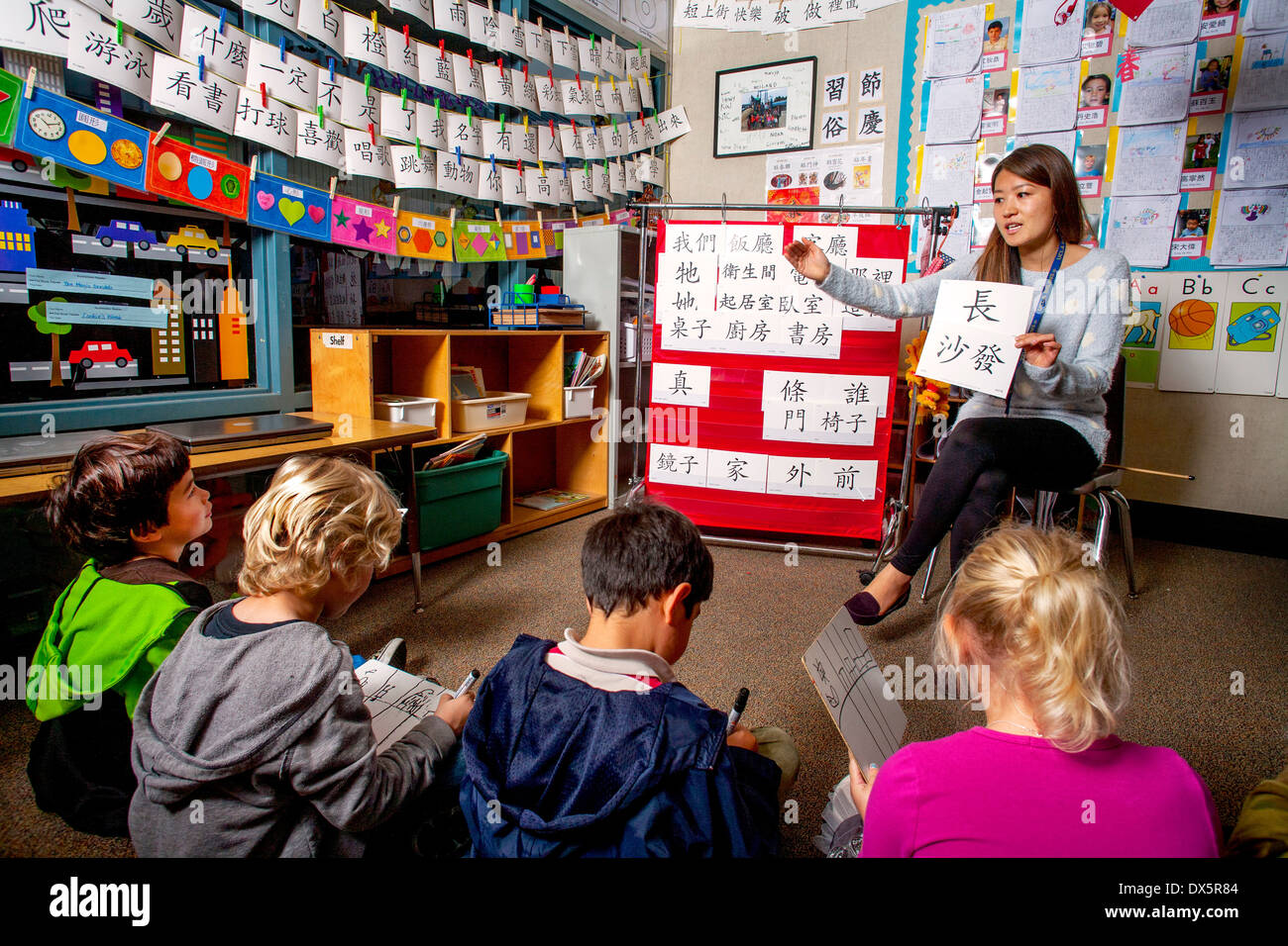 An Asian American teacher conducts a first grade Mandarin Chinese language class in Laguna Niguel, CA. Note Chinese characters and dragon puppet. Stock Photo