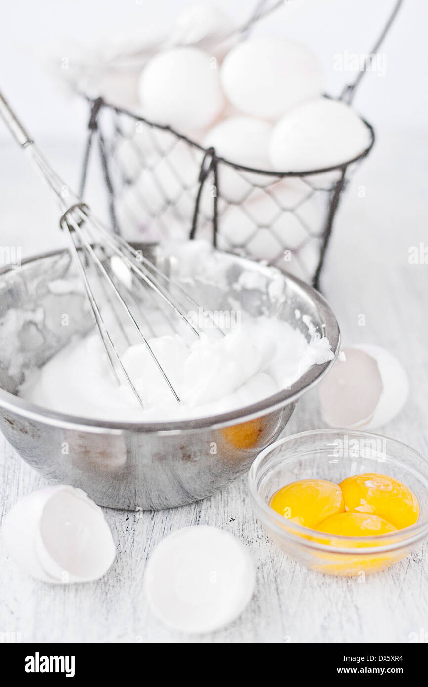 Whisked egg whites in stainless bowl, egg shells, yolks and egg in