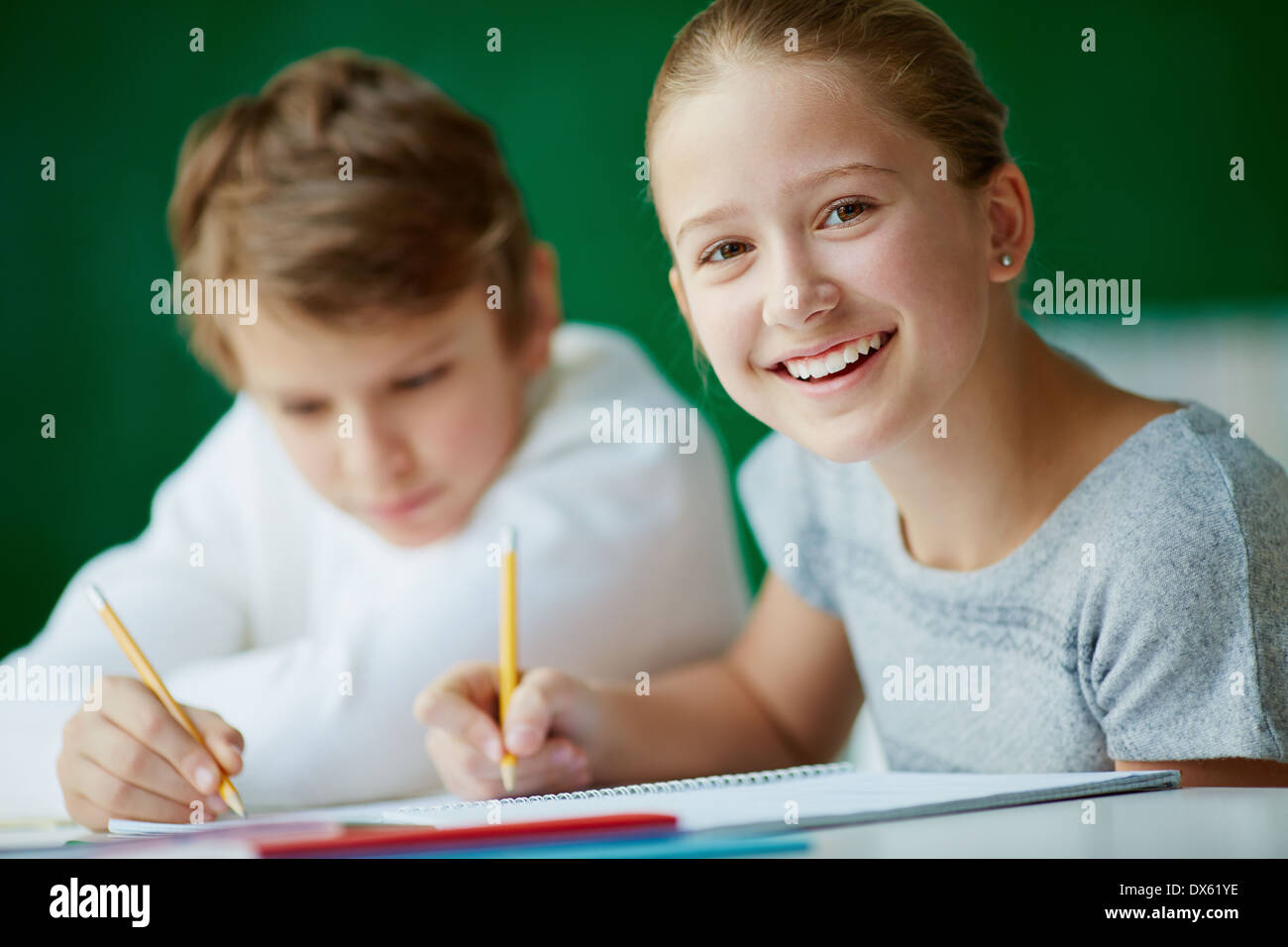 Portrait of cute schoolgirl looking at camera while drawing at lesson ...