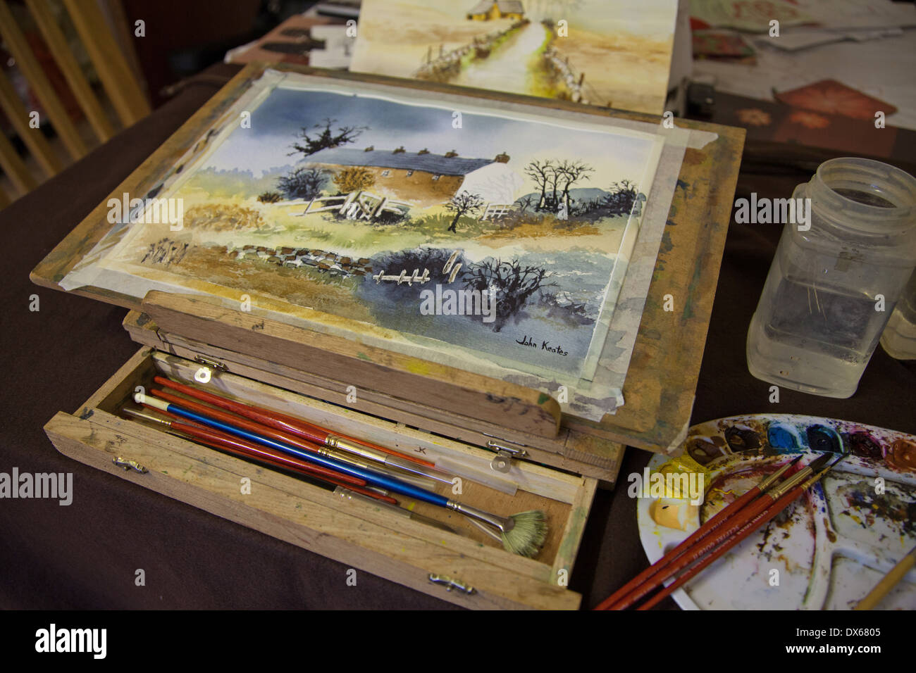 A watercolour painting on a table easel with a palette brushes and water containers Stock Photo