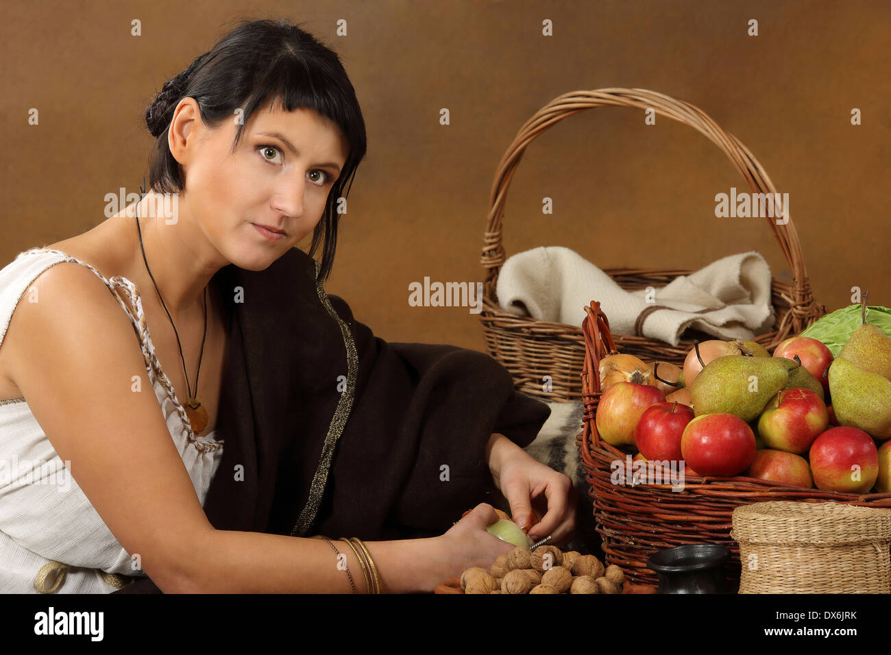 Young Romana peeling the onion with basket full of fruits and vegetables. Concept studio portrait on brown background. Stock Photo